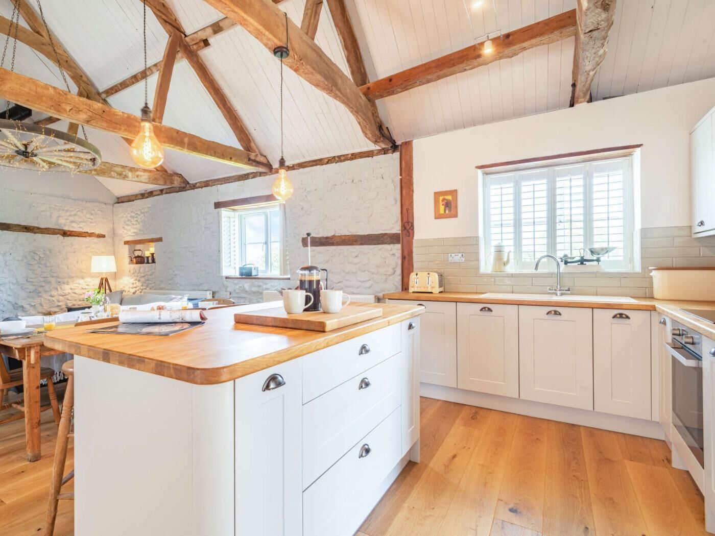A rustic kitchen with exposed wooden beams, a central island with a coffee maker, and a window with a view.