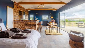 A bedroom with a large bed, a wooden bar, a dining area, and a balcony with a view. - 1 Bed in Abergavenny (oc-88015) (Llanover)