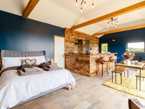 A bedroom with a large bed, a wooden bar area, and a dining space with chairs.