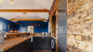 A modern kitchen with dark cabinetry, a wooden accent wall, and a built-in oven. - 1 Bed in Abergavenny (oc-88015) (Llanover)