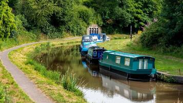 A narrow waterway with boats docked on the right, a pathway on the left, and dense greenery in the background.