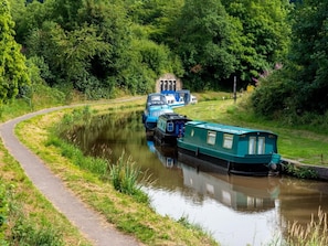 A narrow waterway with boats docked on the right, a pathway on the left, and dense greenery in the background.