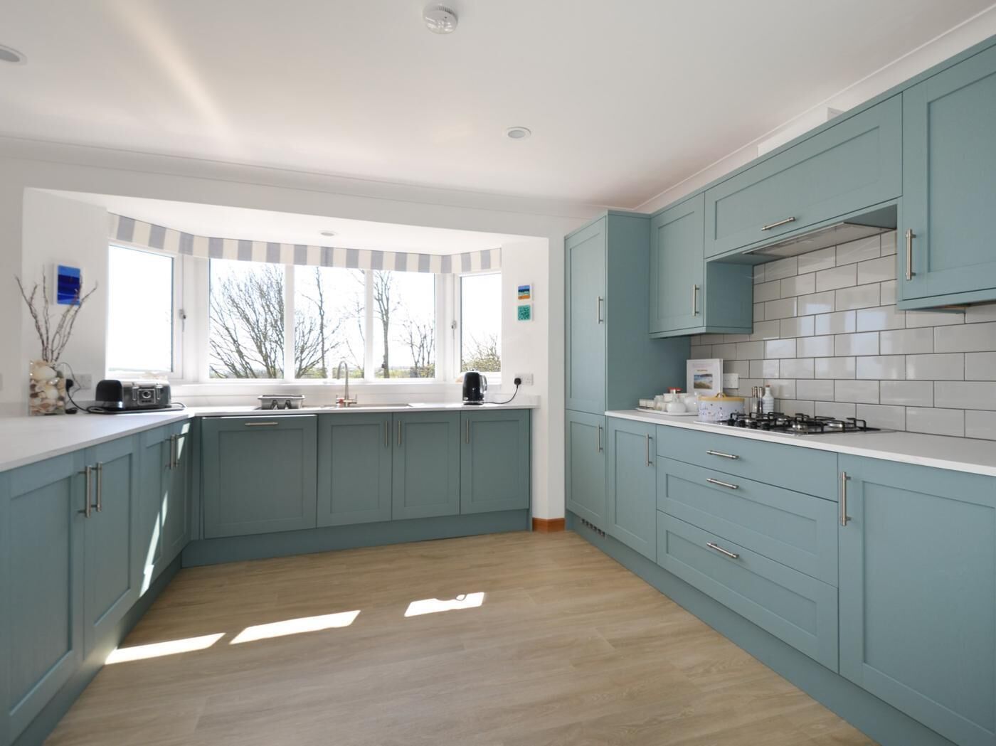 Una cucina moderna con mobili color petrolio, un piano di lavoro bianco e un'ampia finestra che lascia entrare la luce naturale.