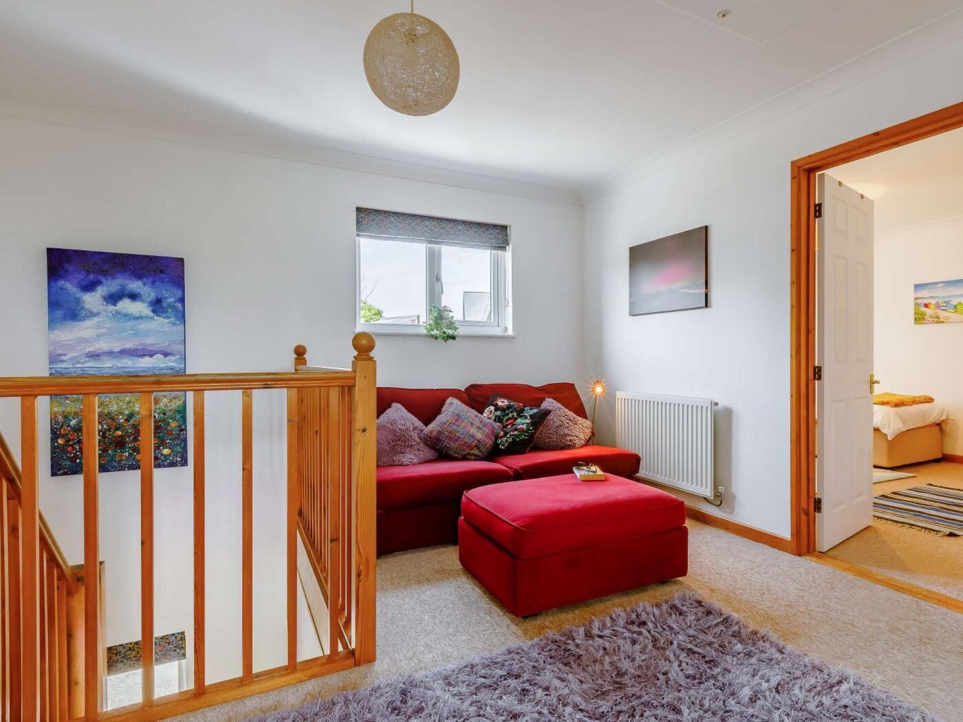 Een kamer met een rode bank, een houten trap, een raam met uitzicht en een radiator.
