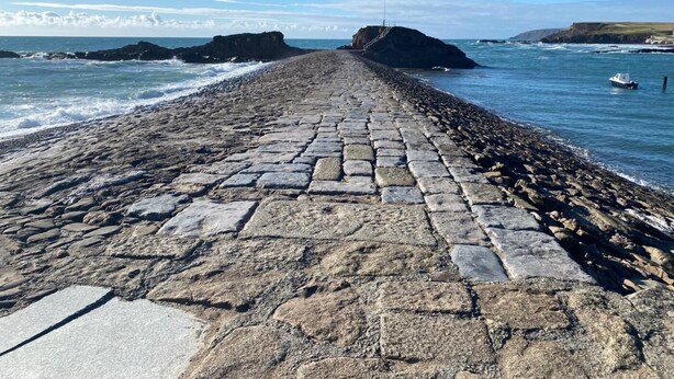 Ein Pflasterweg führt zum Meer, begleitet von Felsformationen an beiden Seiten.