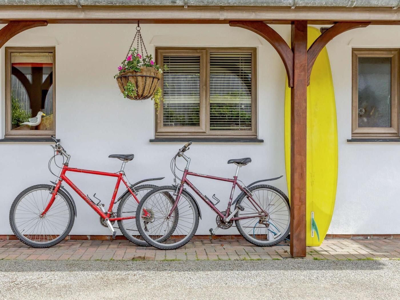 Due biciclette parcheggiate sotto un portico con un surf leantto al muro.