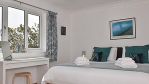 Ein Schlafzimmer mit einem Bett, einem Schreibtisch, einem Stuhl, einem Fenster mit Vorhängen und einem gerahmten Bild an der Wand.