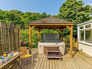 A wooden deck with a covered hot tub, a table with breakfast items, and a chair. - 2 Bed in Saltash (oc-88308) (Notter)
