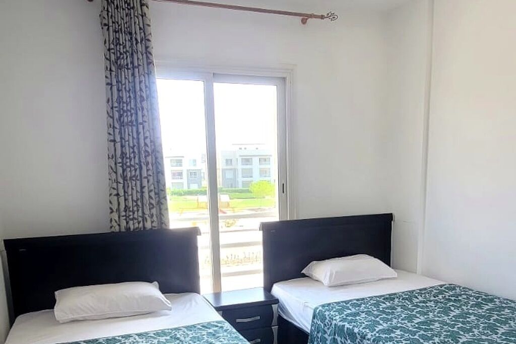 A hotel room with two beds, a window with a view of buildings, and a curtain.