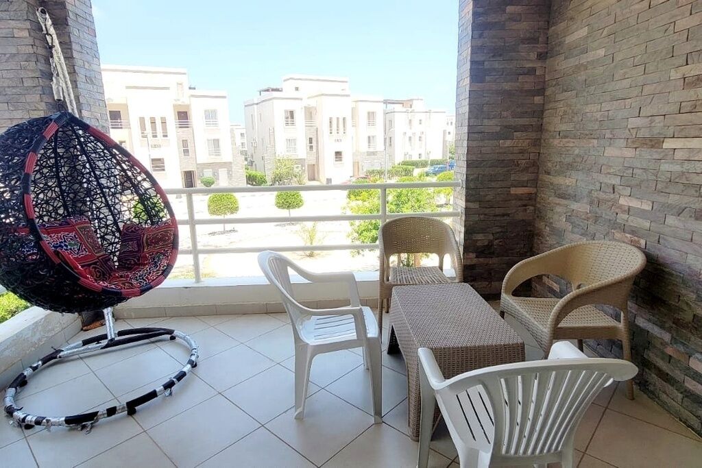Un balcón con una mesa y sillas de mimbre, una silla colgante y vistas a edificios.
