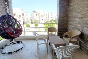 A balcony with a wicker table and chairs, a hanging chair, and a view of buildings. - AMWAJ - 2 bedroom chalet with poolview (Marsa Matrouh Governorate)