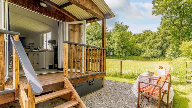 Ett trähus med en inglasad veranda, ett matbord med stolar och en uteplats med grusbeläggning.