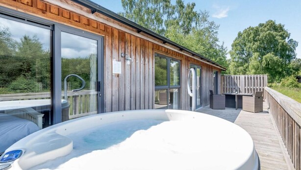 A wooden cabin with a hot tub, glass doors, and a deck.