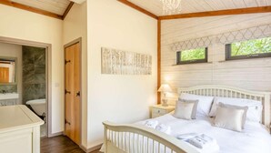 A bedroom with a wooden bed, a nightstand with a lamp, a wall-mounted artwork, and a window with a view of greenery.