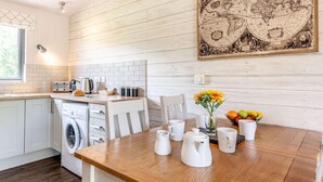 A kitchen with a washing machine, a coffee maker, and a fruit bowl on the table.