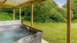 Een hottub onder een houten pergola, met een gazon en bomen op de achtergrond.