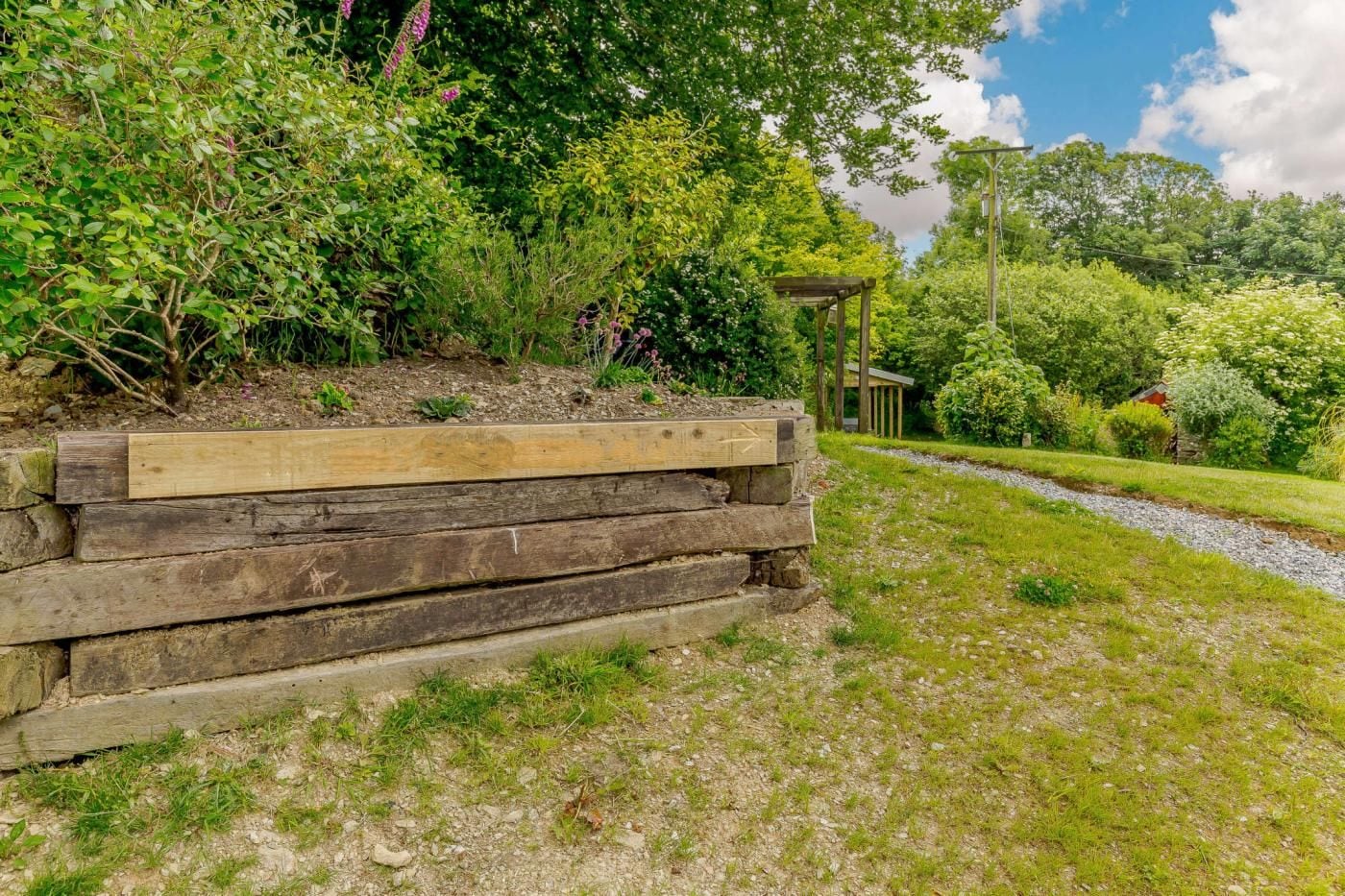 A garden with a wooden bench, a stone wall, and a pathway leading to a gazebo.