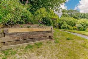 A garden with a wooden bench, a stone wall, and a pathway leading to a gazebo.