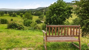Un banc en bois, installé dans un champ verdoyant, d’où l’on peut admirer des collines ondulantes et des arbres.