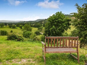A wooden bench in a grassy field with a view of rolling hills and trees. - 1 Bed in Bala (oc-88450) (Llandderfel)