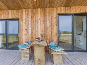 A wooden deck with a table and benches, a glass door, and a view of the outdoors.