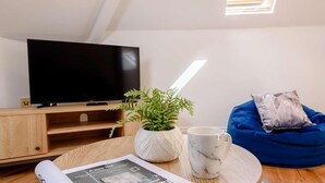 Ein modernes Wohnzimmer mit Flachbildfernseher, Couchtisch aus Holz, blauem Sitzsack, Topfpflanze, Marmormug und einer Zeitschrift.