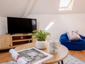 A modern living room with a flat-screen TV, a wooden coffee table, a blue bean bag, a potted plant, a marble mug, and a magazine. - 1 Bed in Tenby (oc-88504) (Tenby)