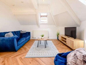 A loft-style living room with a blue sofa, a wooden coffee table, a TV on a wooden stand, and a patterned rug. - 1 Bed in Tenby (oc-88504) (Tenby)