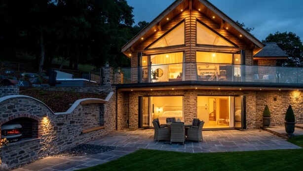 A modern two-story house with a stone exterior, a balcony, and a patio with outdoor furniture.