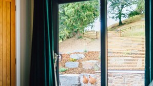 A room with a large window, a bed, and a view of a stone wall with chickens outside.