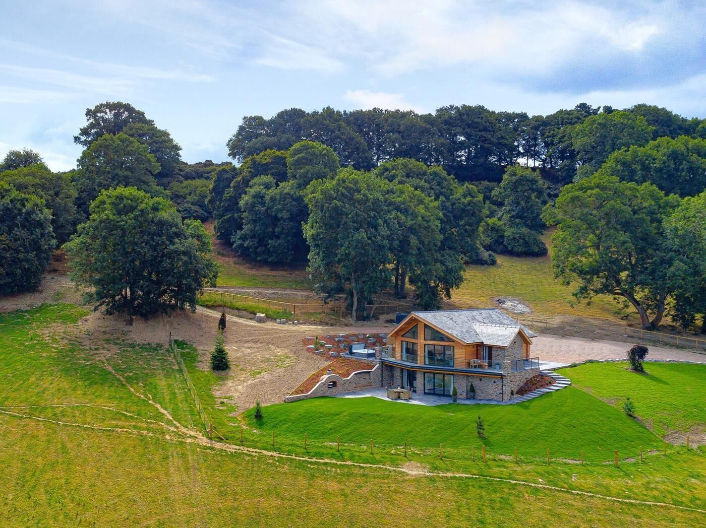 Una casa moderna con cimientos de piedra y estructura superior de madera, rodeada de exuberante vegetación y árboles.