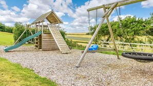 Ein Spielplatz mit einer Holzrutsche, Schaukeln und einem kleinen Schutzhaus.