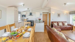 Eine moderne Küche mit einer zentralen Kochinsel, ein Essbereich mit Holztisch, gedeckt für das Frühstück, und ein Wohnbereich mit einer Ledersofa.