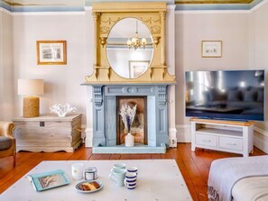 A living room with a fireplace, a television, and a coffee table with books and cups. - 4 Bed in East Cowes (oc-88655) (East Cowes)