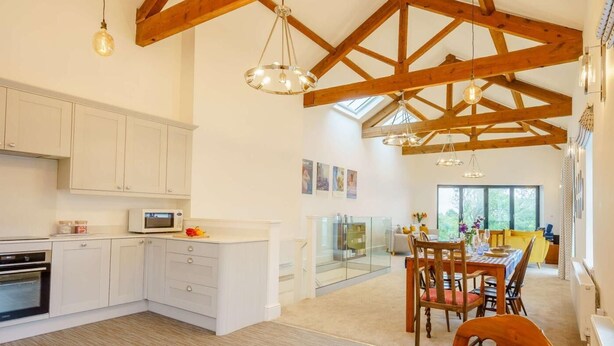 A spacious kitchen with white cabinets, a dining area with a wooden table and chairs, and a high ceiling with exposed wooden beams. - 2 Bed in Askam-in-furness (oc-88651) (Kirkby Ireleth)