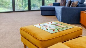 A living room with a large window, a blue sofa, and a yellow ottoman with a board game. - 2 Bed in Askam-in-furness (oc-88651) (Kirkby Ireleth)