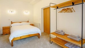 A bedroom with a wooden bed, bedside tables, a wooden wardrobe, and a hanging clothes rack with towels. - 2 Bed in Askam-in-furness (oc-88651) (Kirkby Ireleth)