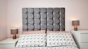 Una cama con cabecera capitonada, dos lámparas de noche y una colcha estampada.