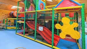 Zona de juegos con un tobogán, estructuras para escalar y un recinto cubierto con red.
