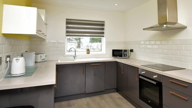 Una cocina moderna con gabinetes grises, una campana extractora de acero inoxidable, un microondas y un ventanal con persianas.