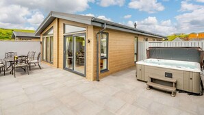 Ein modernes Haus mit einer Terrasse, einem Whirlpool und einem Essbereich mit Gartenmöbeln.
