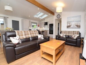 A modern living room with a brown leather sofa, a wooden coffee table, and a kitchen in the background. - 2 Bed in Newton Stewart (oc-88645) (Auchenmalg)