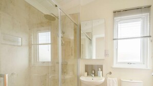 Ein Badezimmer mit einer Duschkabine, einem Standwaschbecken, einer Toilette und einem Fenster mit Jalousien.