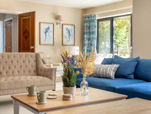 A living room with a beige sofa, a blue sofa, a coffee table with decorative items, and framed artwork on the wall. - 5 Bed in Lymington (oc-88733) (Everton)