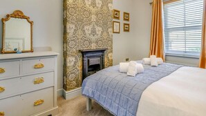A bedroom with a fireplace, a bed with a blue quilt, a white dresser with gold handles, and a window with curtains. - 2 Bed in Bakewell (oc-88661) (Bakewell)