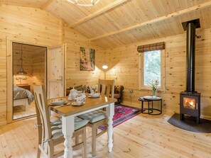 A wooden cabin interior with a dining area, a fireplace, and a window with a view of trees. - 1 Bed in Shrewsbury (oc-88768) (Leighton)