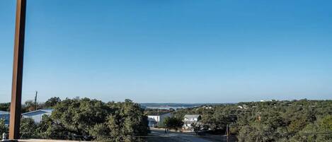 A balcony with a clear view of a residential area, trees, and a distant body of water.