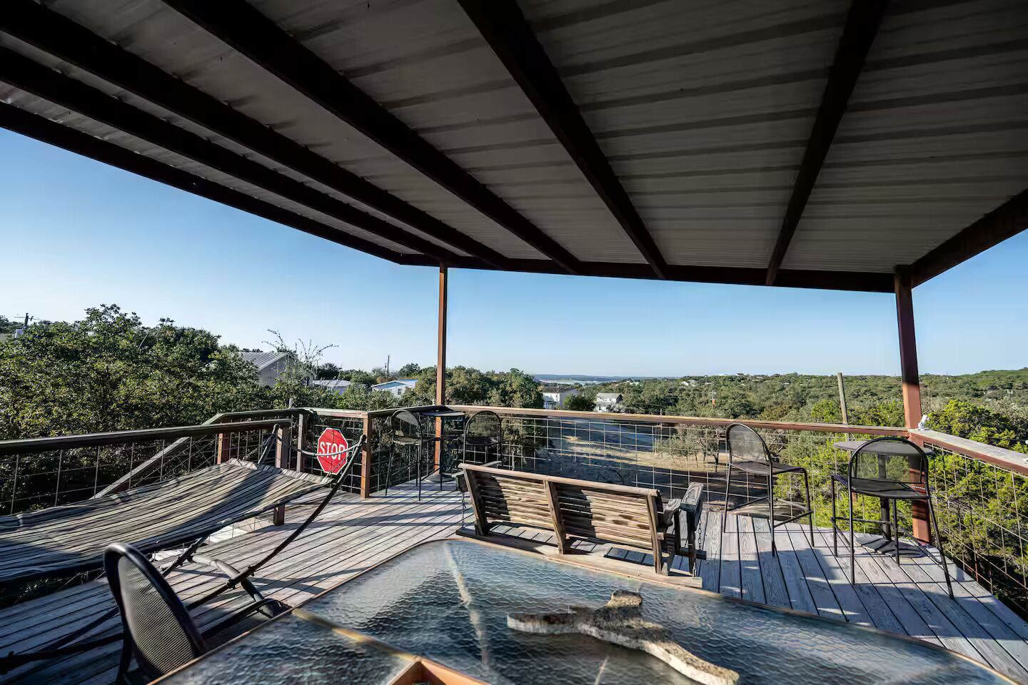 A covered outdoor deck with wooden benches and a stop sign, overlooking a scenic landscape.
