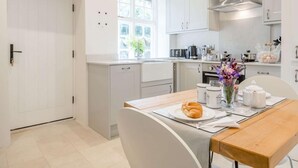 A modern kitchen with white cabinets, a stainless steel range hood, a window with a view, and a dining area with a table set for two. - 1 Bed in Brecon (oc-88748) (Trallong)