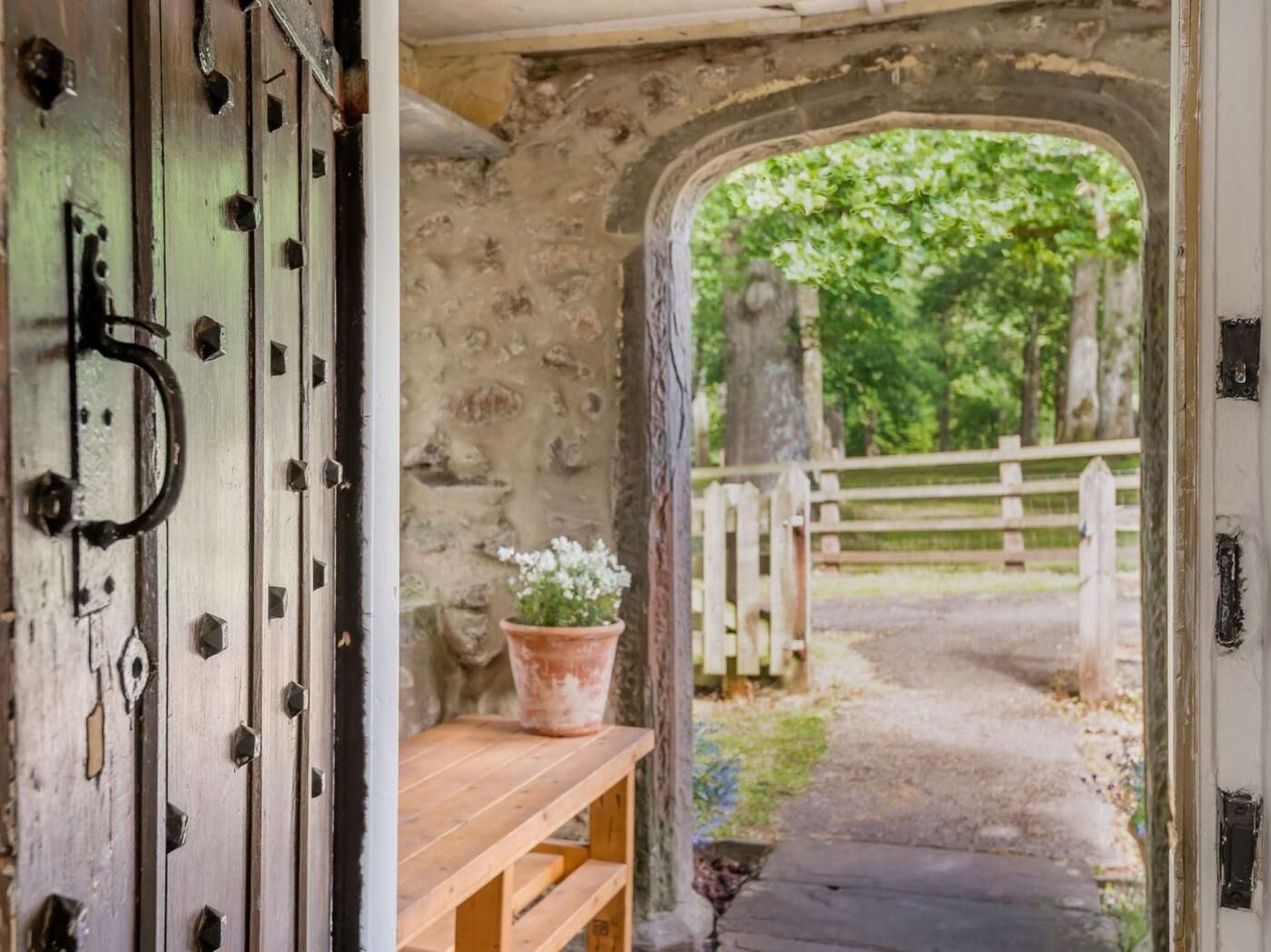 An arched doorway leading to a garden with a wooden bench and a potted plant.